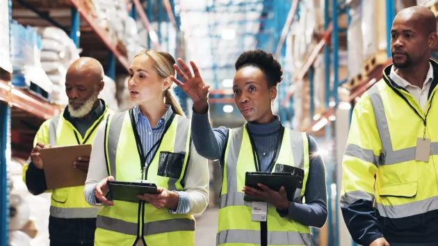 4 people wearing high visibility jackets looking at digital devices