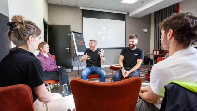 people in a meeting room, sat on red chairs
