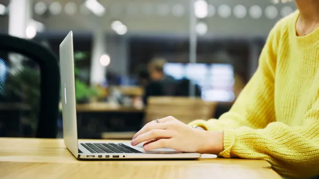 person in an office wearing a yellow jumper using a laptop