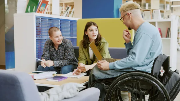 Wheelchair user in a library chatting to friends