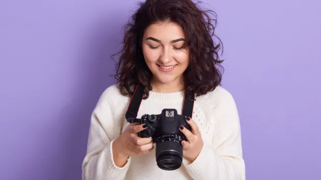Indoor studio shot of photographer holding her camera in both hands, looking at photos.