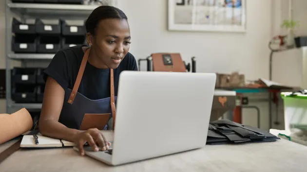 female leather worker using a laptop at a workbench