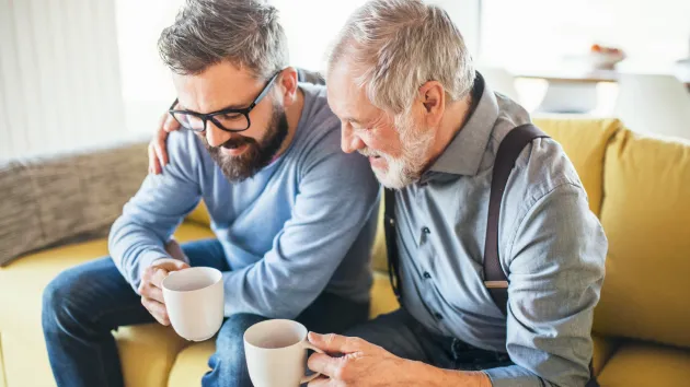 Grandfather and grandson sitting on a settee drinking coffee