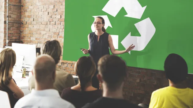 People listening to a speaker, recycling symbol in the background
