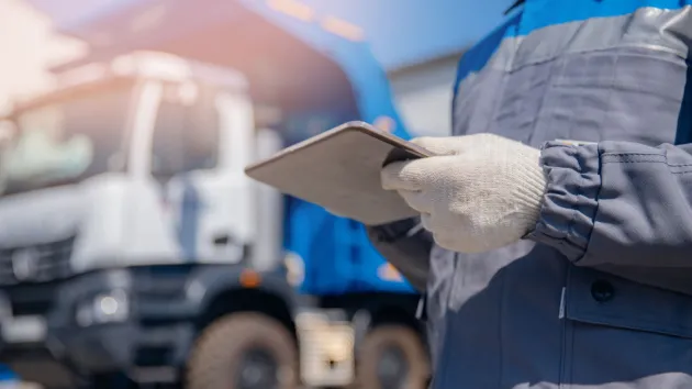 Dump truck driver man in uniform with tablet computer controls loading of cargo