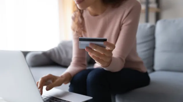 Person using a laptop and paying for a service with a bank card.