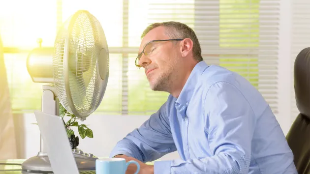 man working in an office sat next to a fan - hot day