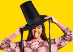 Woman wearing a tall Welsh hat and pink traditional Welsh jumper on a yellow background. 