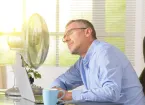 man working in an office sat next to a fan - hot day 