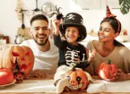  parents with son smiling while creating jack o lantern from pumpkin during Halloween celebration in kitchen at home