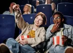 Young woman and her friend spending time together at cinema watching movie and eating popcorn